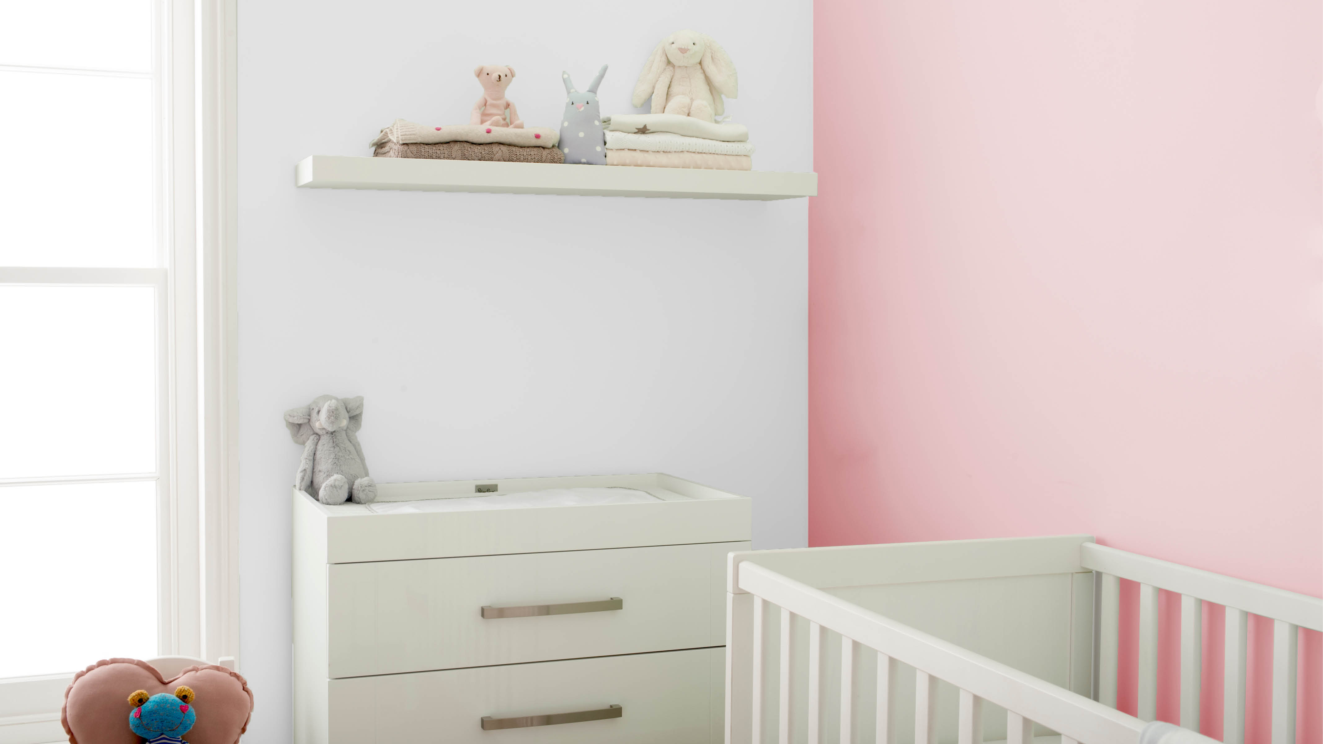 Habitación de bebé rosa con estantes flotantes Un armario blanco y un conjunto de estantes flotantes son un fantástico lugar para colocar peluches y otros objetos del bebé.